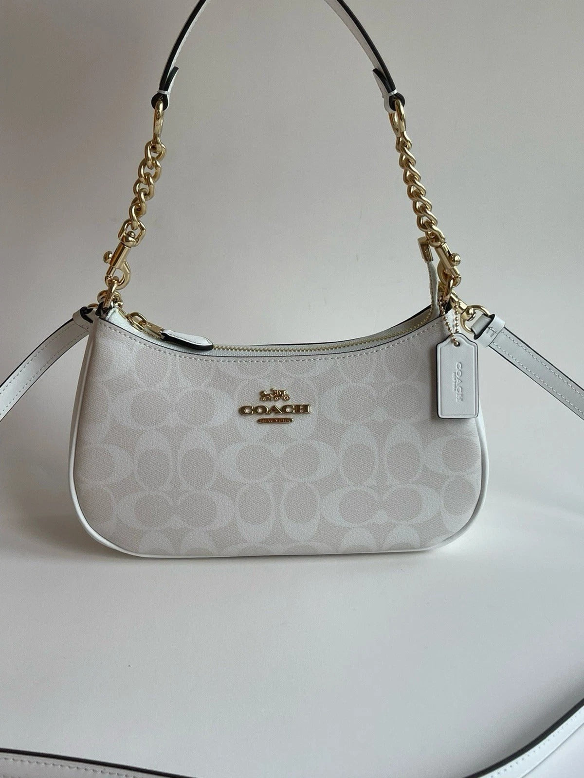 White Coach signature-style shoulder bag with gold-tone chain-detail shoulder strap, detachable long strap, zipper closure, and logo tag.