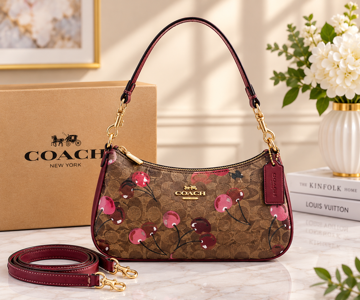 Brown Coach signature-style shoulder bag with cherry-print detailing, burgundy trim, gold-tone hardware, and a detachable long strap.