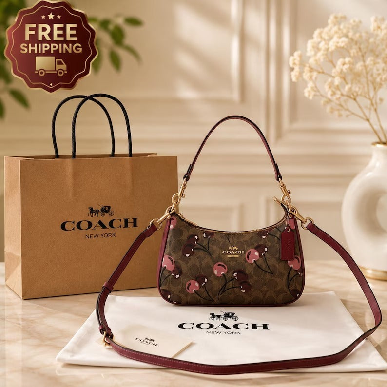 Brown Coach signature-style shoulder bag with cherry-print detailing, burgundy trim, gold-tone hardware, and a detachable long strap.