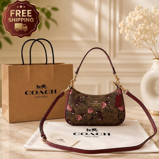 Brown Coach signature-style shoulder bag with cherry-print detailing, burgundy trim, gold-tone hardware, and a detachable long strap.